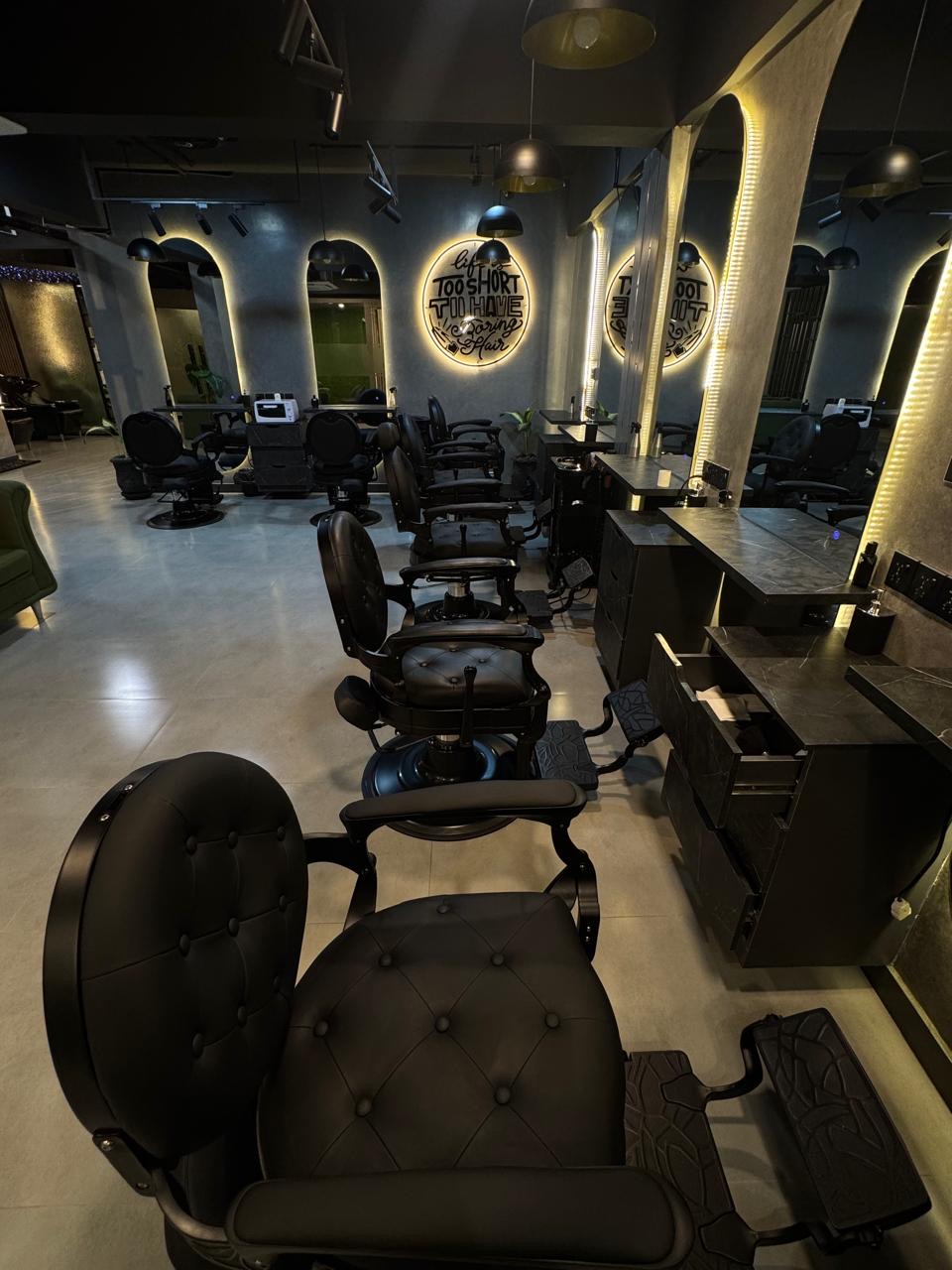 Row of black leather barber chairs facing arched backlit mirrors inside The Man Redefined salon