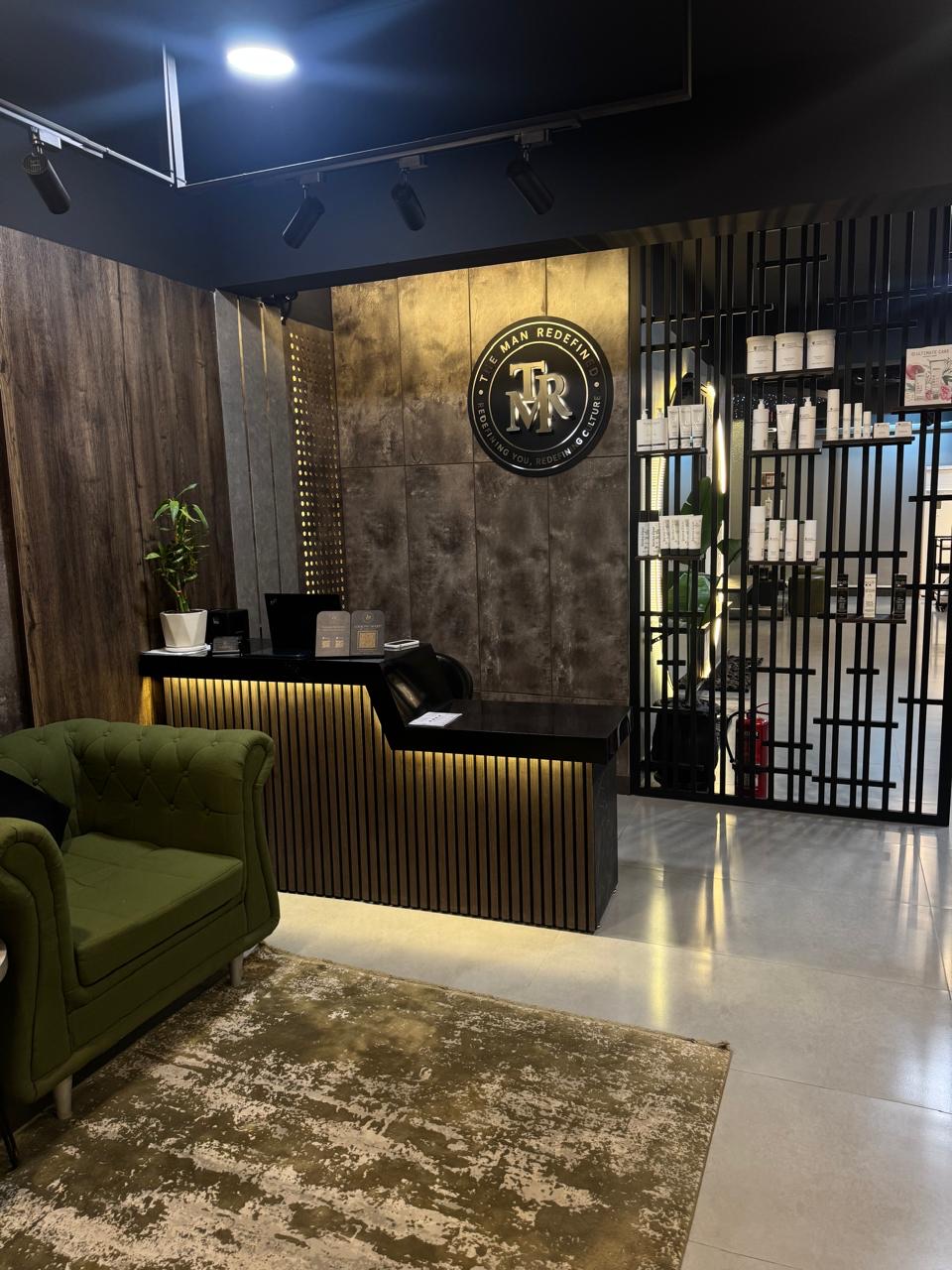 Reception desk with the illuminated TMR logo and a green velvet armchair at The Man Redefined